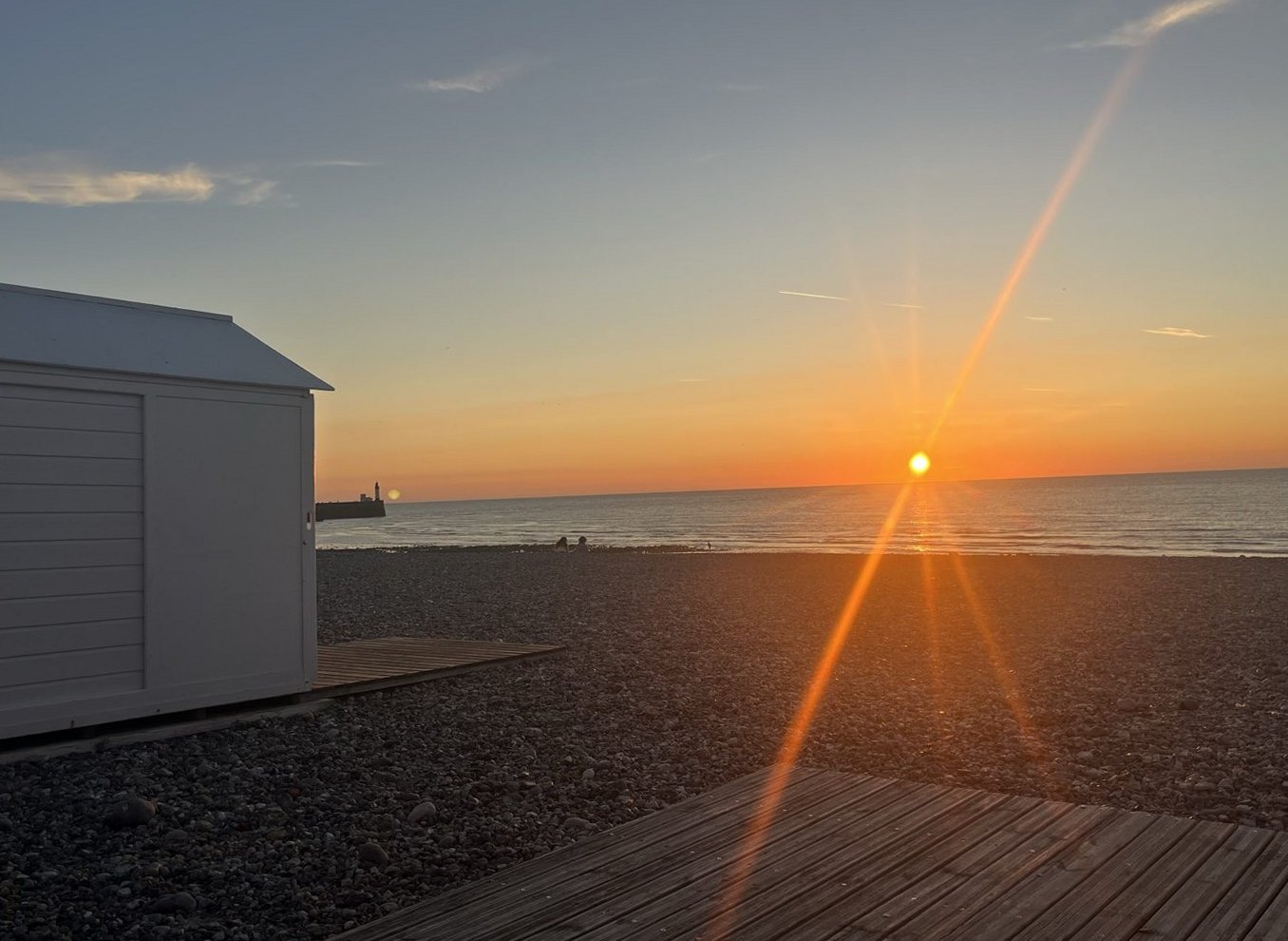Cabine de plage au coucher du soleil, phare au loin
